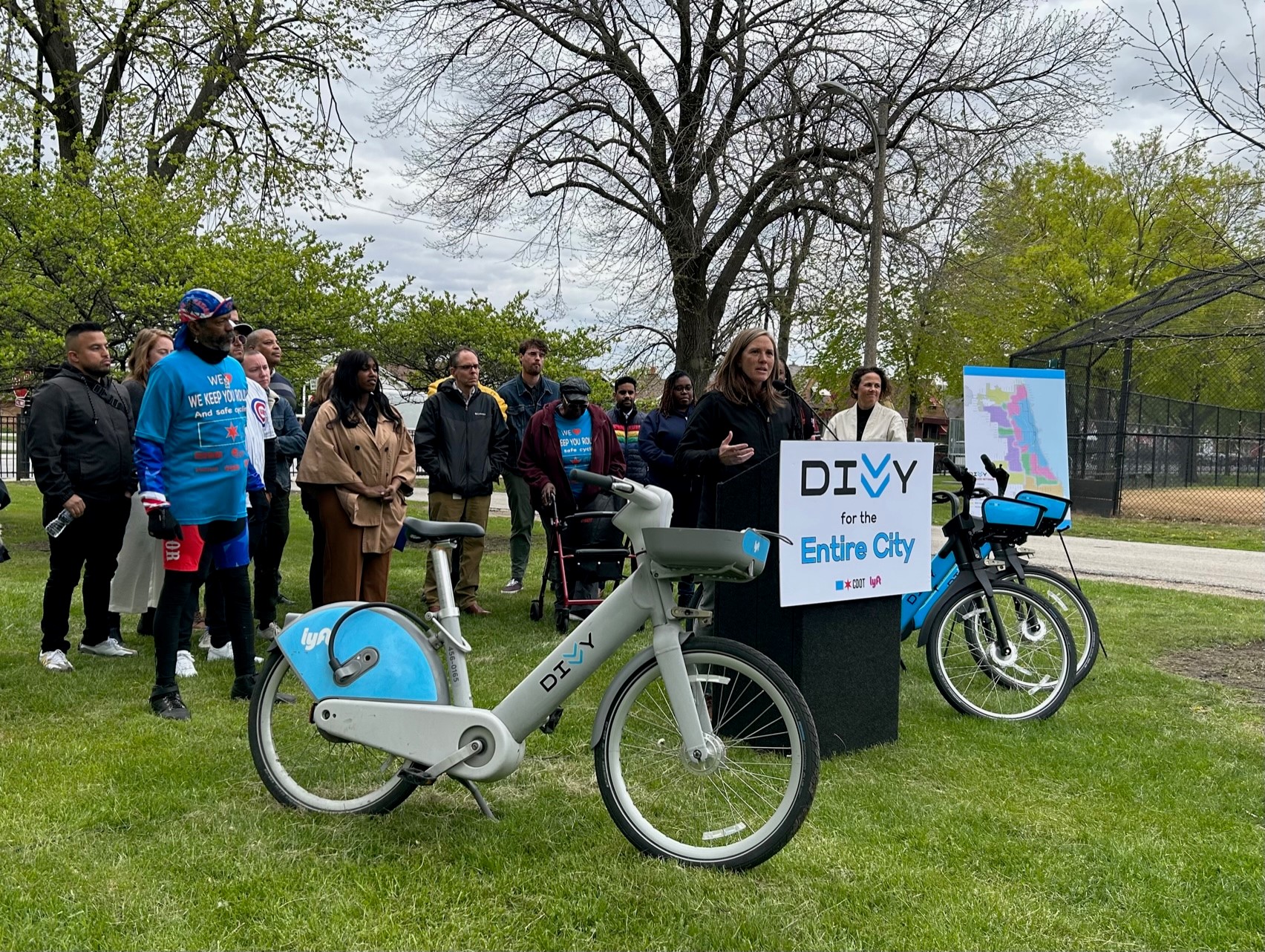 CDOT Commissioner Gia Biagi standing behind a podium, surrounded by community members and Divvy Bikes